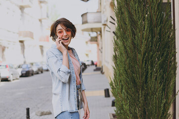 Back side view young surprised happy woman in casual jeans clothes eyeglasses talk speak by mobile cell phone strolling walk go down city street outdoors People youth active urban lifestyle concept.