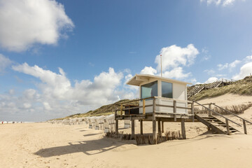 empty beach chairs standing on an empty beach just behind a dune and a wooden jetty with an...