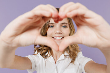 Little kid girl 12-13 years old in white shirt showing shape heart with hands look through close up heart-shape sign isolated on purple background children studio portrait Childhood lifestyle concept
