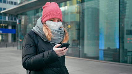 Casual Woman in Surgical Face Mask and Gloves Uses Mobile App on Smartphone Walking Outdside in City Street. COVID-19 Coronavirus Pandemic Outbreak