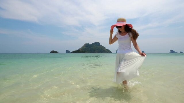 Woman walk at ankle-deep waves along sea beach at beautiful tropical island. Tourist lady at long holidays in Thailand, recreate and have tour around exotic islands