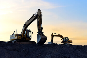 Excavator working on earthmoving at open pit mining on sunset background. Backhoe digs sand and...