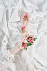 Female hands holding tiny tender pink daisy flowers, one of them applied to hand with patch on white background, top view with copy space. Creative spring floral aesthetics concept. High quality photo