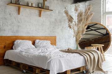 Closeup view on spacious airy white eco style loft bedroom with bed,  mirror and pampas grass decoration