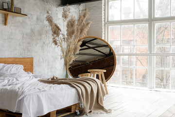 Side closeup view on spacious airy white eco style loft bedroom with bed,  mirror and pampas grass decoration