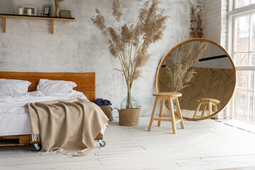 Side closeup view on spacious white eco style loft bedroom with bed,  mirror and pampas grass...