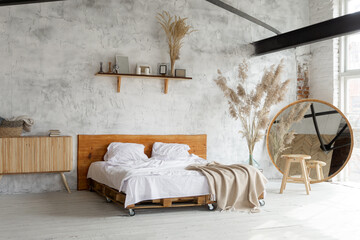 Side view of pacious airy white industrial loft bedroom with bed,  mirror and pampas grass decoration