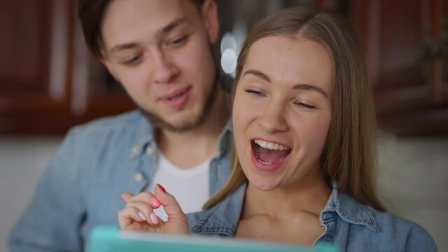 Close-up portrait of cheerful millennial Caucasian couple gossiping surfing social media on tablet at home. Laughing joyful man and woman talking smiling enjoying time together. Lifestyle concept