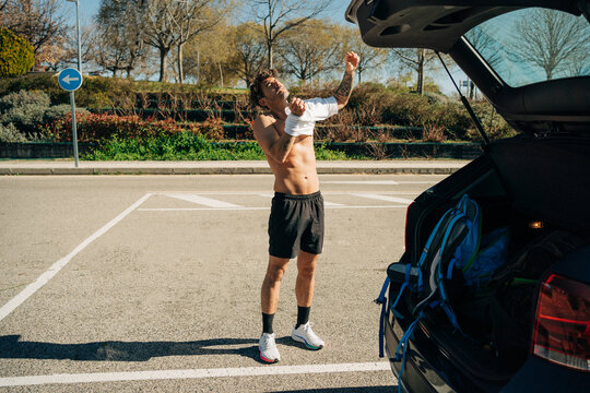Muscular sportsman putting on t shirt against car