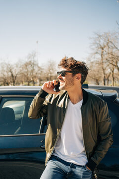 Cheerful man talking on smartphone near car