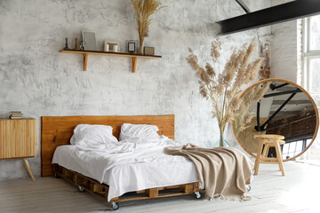 Spacious airy white eco style loft bedroom with bed,  mirror and pampas grass decoration