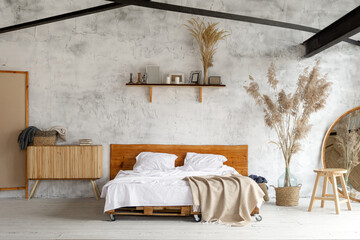 Spacious airy white industrial loft bedroom with bed,  mirror and pampas grass decoration