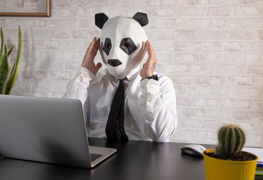 Unrecognizable exhausted businessman in panda mask against laptop in office