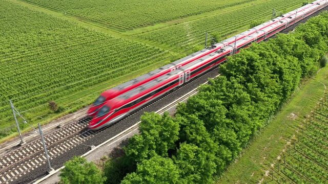 Two high-speed trains of red color moving towards the aerial view. The movement of trains between the vineyards top view.