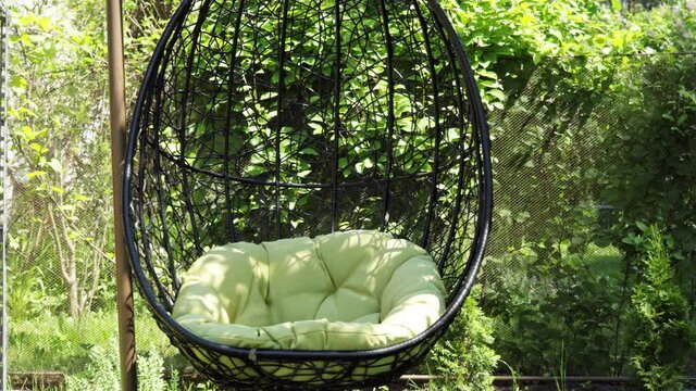 Coccoon chair sways in the wind  outside in the garden. Green nature and comfy sitting place.