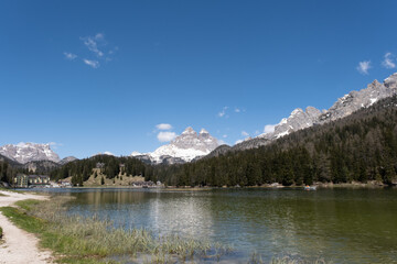 Fototapeta na wymiar Misurina, Italy - May 31, 2021: The fabulous alpine lake in the Dolomites. Boat on the water. Lovely and relaxing place in the Italian Alps. Reflections in the rippled water. Sunny spring day.