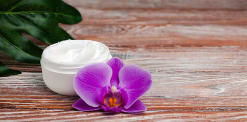 Jar of face cream and orchid on wooden background. Natural skincare cosmetics. Beauty and health concept. Close-up. Copy space.