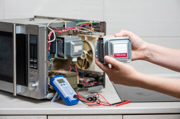 Repair of the microwave oven. The woman shows the new magnetron.