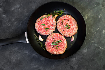 Raw beef meat burger steak cutlets in the pan on the black table.
