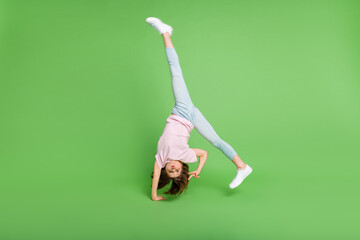 Full size photo of young girl handstand balance show peace cool v-sign isolated over green color...