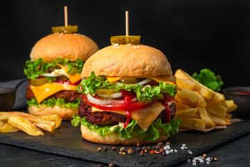 Two large juicy hamburgers and French fries on a black background. Fast food. Horizontal view, close-up.