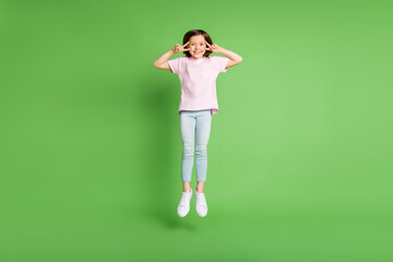 Full body photo of young girl happy positive smile jump up show peace cool v-sign isolated over green color background