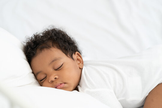 black african american baby sleeping on a white mattress.