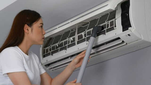 Young woman using vacuum cleaner to cleaning the air conditioner at home
