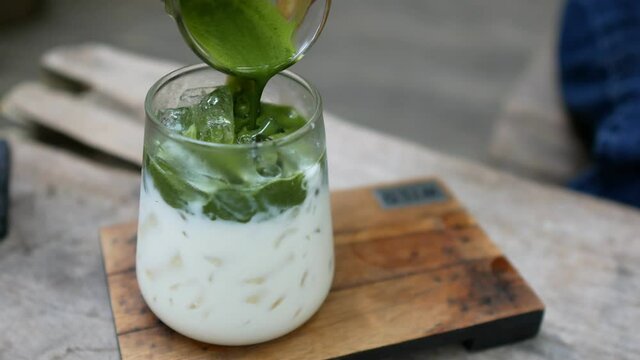 The concentrated matcha green tea is being poured into fresh milk with a small lump of water at cafe'