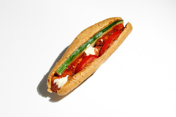 Greek hot dog with souvlaki, red sauce, tomatoes and cucumber. Street food, hard light. White background