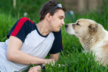 a young man lies on the grass with his dog and both looks into each others eyes