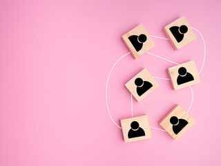 Top view of wooden blocks with black human icons laid scattered on a light pink background, Space for text. Flat lay. ​Teamwork and unity concept