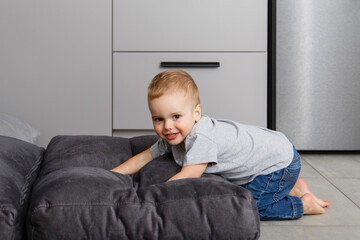 Small baby playing on the floor. Kid of two year old crawls on the floor. Small legs. Toddler baby weared in denim pants smiles to the camera. Child's emotional portrait