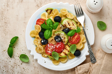 Pasta fiocchi salad with vegetables grilled zucchini, cherry tomato, olives, basil and parmesan cheese in white plate on light slate, stone or concrete background. Lunch concept. Top view