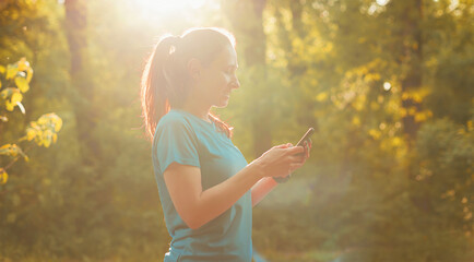 Photo of young sport woman using smartphone app for exercises at sunset