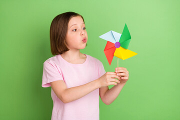 Photo of young little girl blow windmill pinwheel rotate toy isolated over green color background