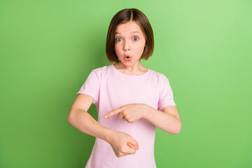 Photo of young little girl amazed shocked surprised point finger hand scar isolated over green...