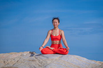 Fototapeta na wymiar Asian young healthy woman posing practice yoga on stone beach with blue cloud sky and sea background in healthy exercise lifestyle concept.