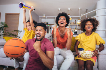 Happy African American family watching tv and cheering basketball games on sofa at home.