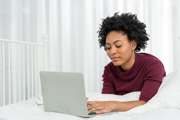 Happy casual beautiful american african woman working on laptop computer while setting  on the bed in the house.
