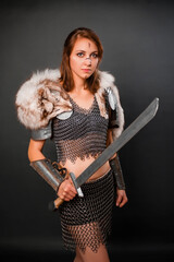 Medieval woman warrior in chain mail armor and polar fox fur on her shoulders standing with a sword in hand on a dark background. Fantasy barbarian, viking.