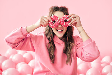 Smiling beautiful woman having fun with donuts over pink background