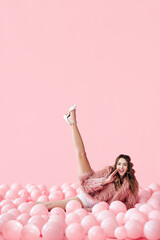 Funny smiling woman lying in many pink balloons with her legs up