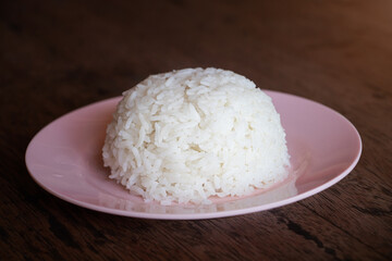 Steam white jasmine rice on pink plate on wooden table. Cooked jasmine rice is a main dish in asia and specially in Thailand.