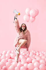 Trendy smiling woman holding megaphone on pink balloons background