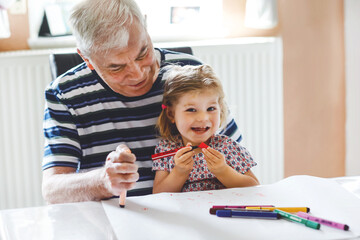 Cute little baby toddler girl and handsome senior grandfather painting with colorful pencils at...