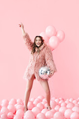 Trendy young woman have fun with party disco ball on pink balloons background