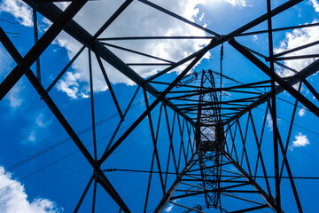 Electric pylons of high voltage lines against a blue sky with white clouds. Photo taken in daylight.