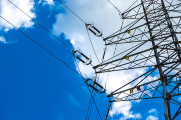 Electric pylons of high voltage lines against a blue sky with white clouds. Photo taken in daylight.