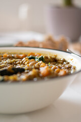 Lentil soup in a white bowl with greens and carrots. Close up of Cooked dish brown color